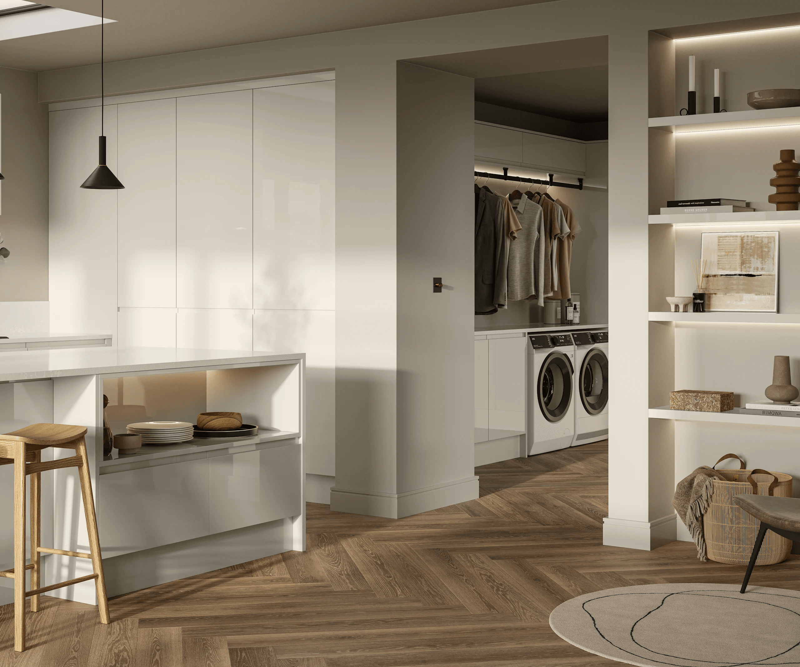 The image shows a modern, bright interior space featuring a kitchen area that seamlessly leads into a laundry room. The kitchen has white glossy cabinets, a white countertop with an open shelf containing plates and wooden items, and a wooden stool. The laundry room visible through an open doorway contains a front-loading washer and dryer with hanging clothes above them. To the right, built-in shelves hold decorative objects, books, and a framed artwork. The floor throughout has a warm herringbone wood pattern, and the lighting is soft, natural with some ambient shelf lighting. The perspective is a wide, eye-level view capturing the open plan and connected functional spaces.