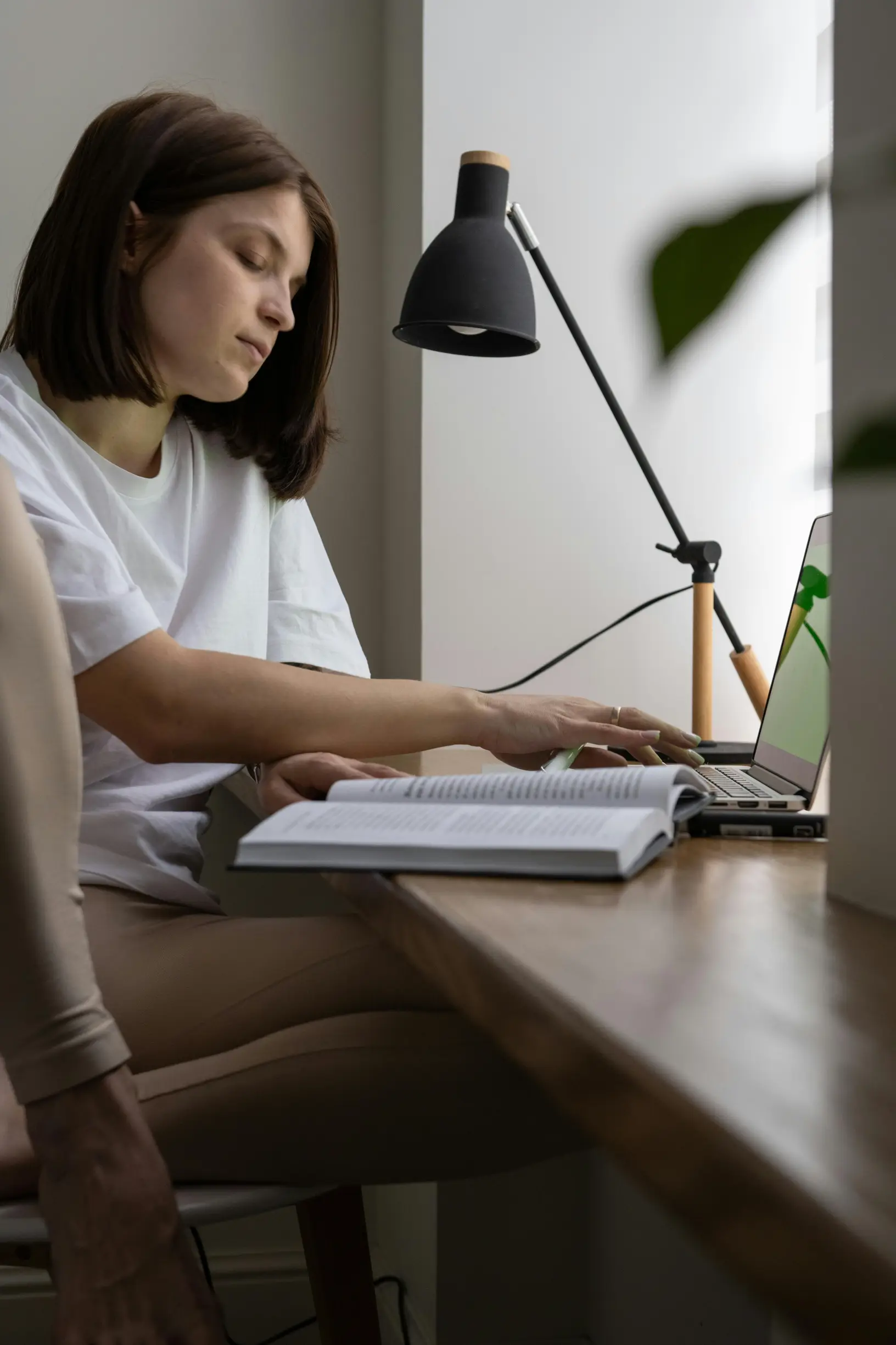 A woman intently studying on her laptop in a home setting, surrounded by books.