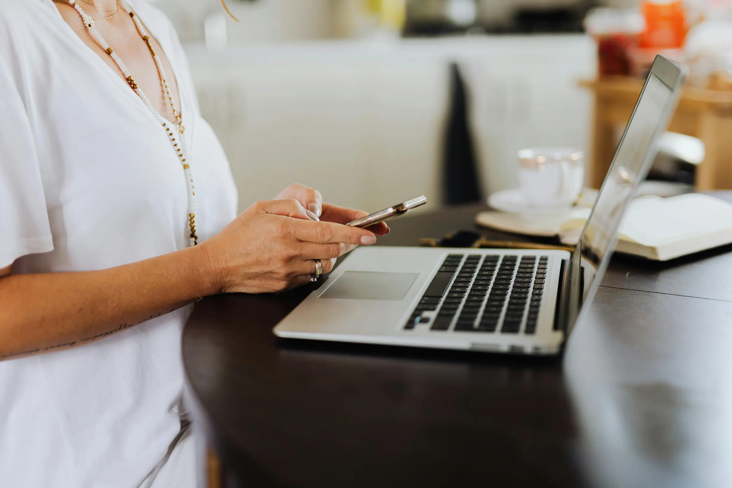 Woman engages with technology using a smartphone and laptop at a home office desk.