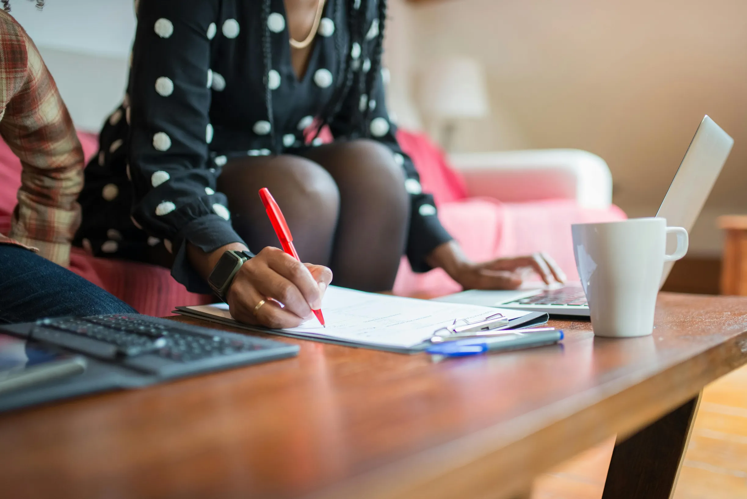Woman taking notes on paper while working on a laptop at home, promoting a freelance environment.