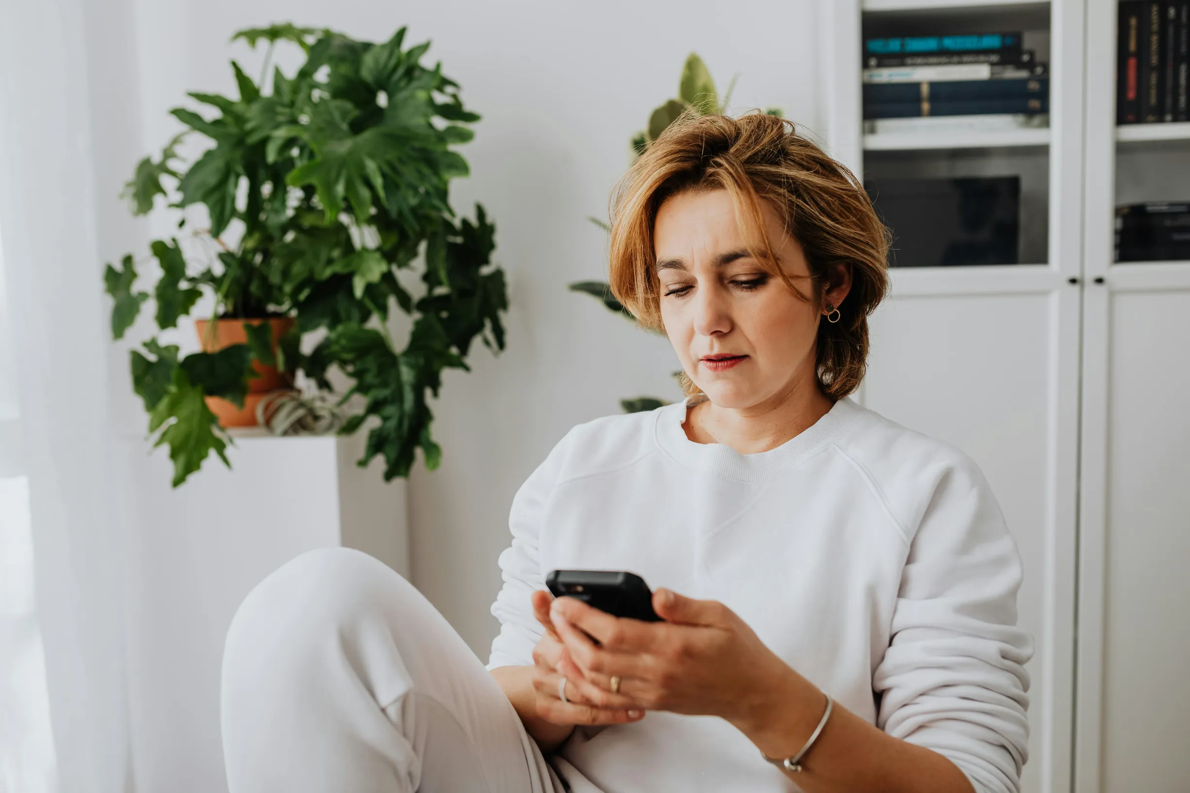 Woman with short hair using smartphone in cozy home setting.