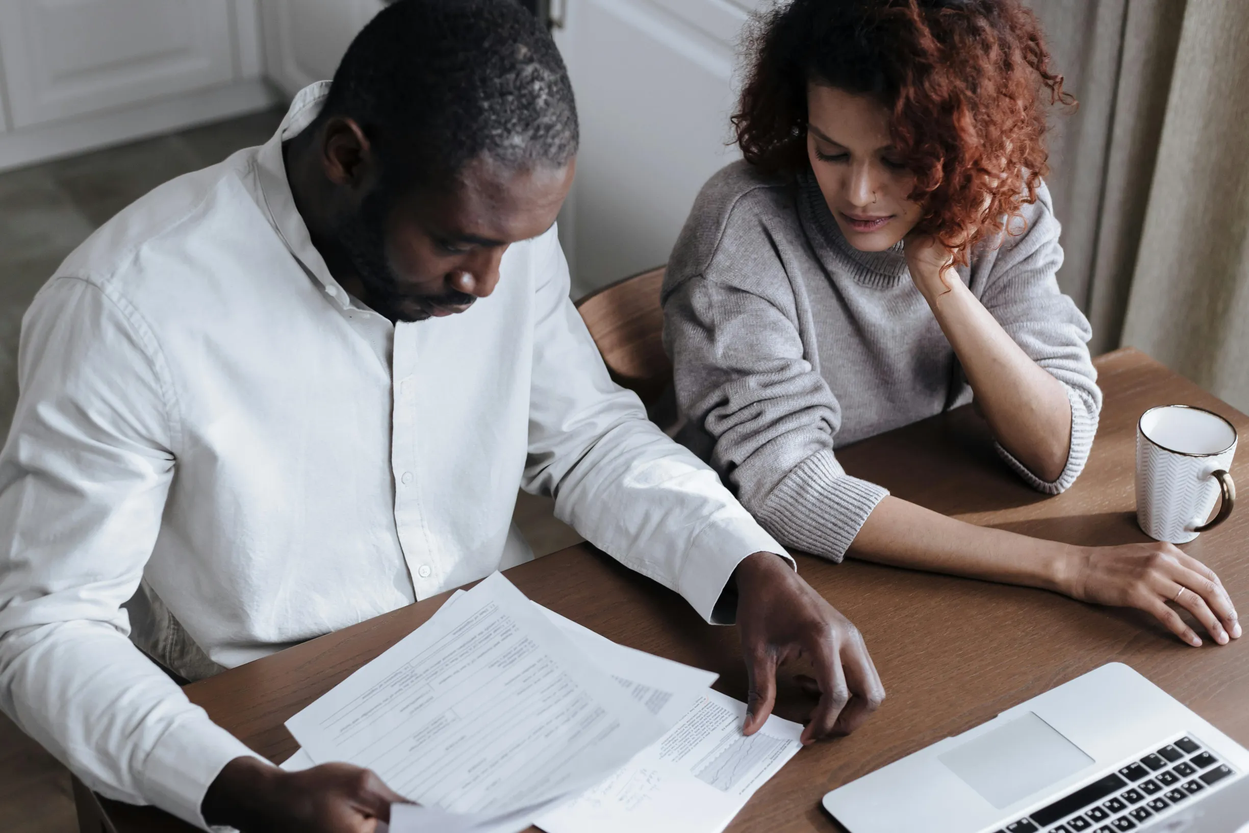 A couple reviews important documents together at a home desk with a laptop.