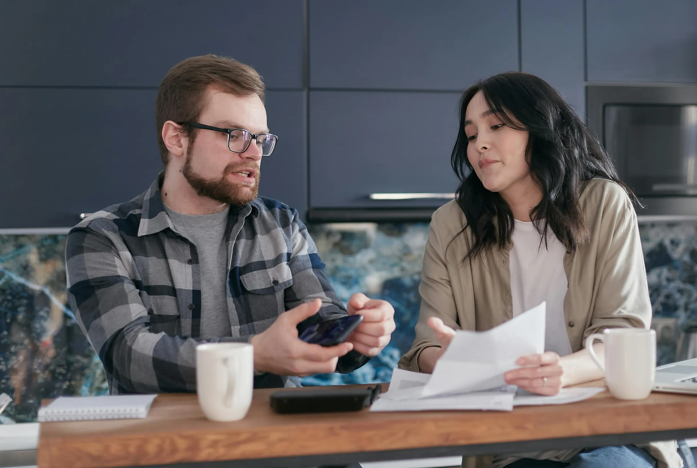 A couple sits at a kitchen table reviewing documents and discussing finances.