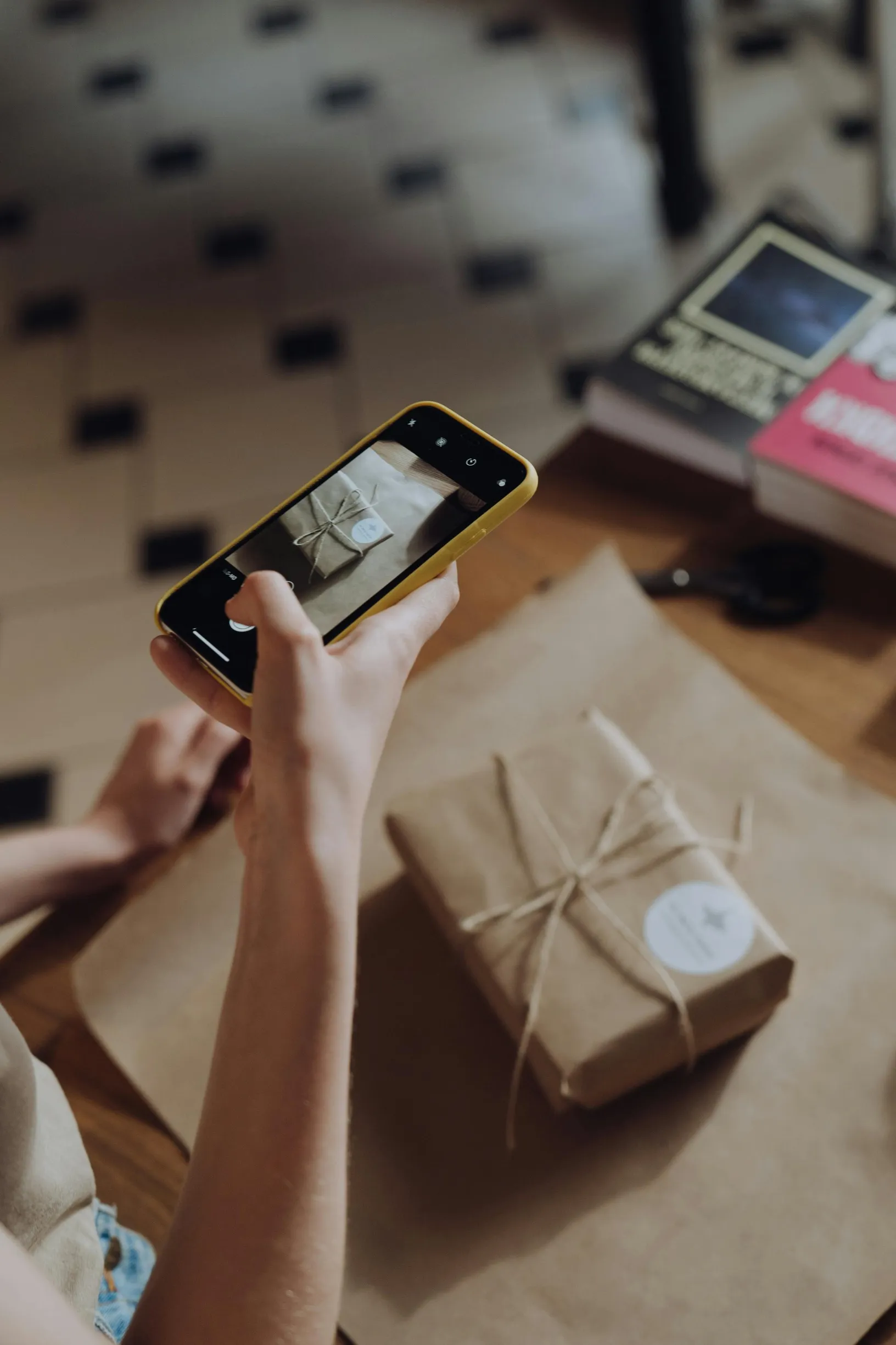A person photographs a wrapped gift with a smartphone indoors.