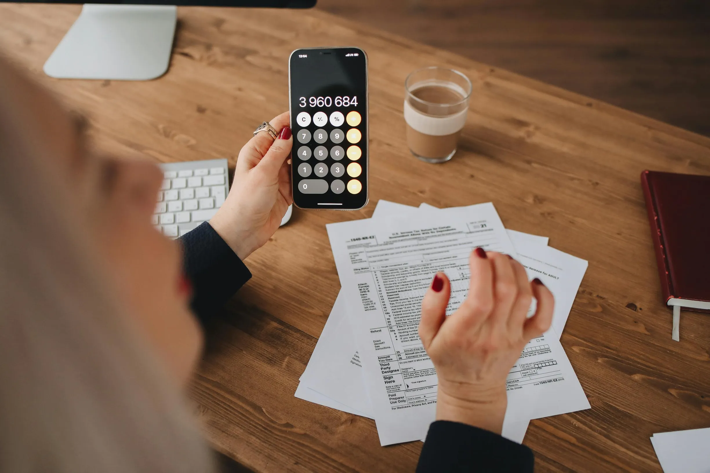 A woman calculates on her smartphone while working with documents at a desk.