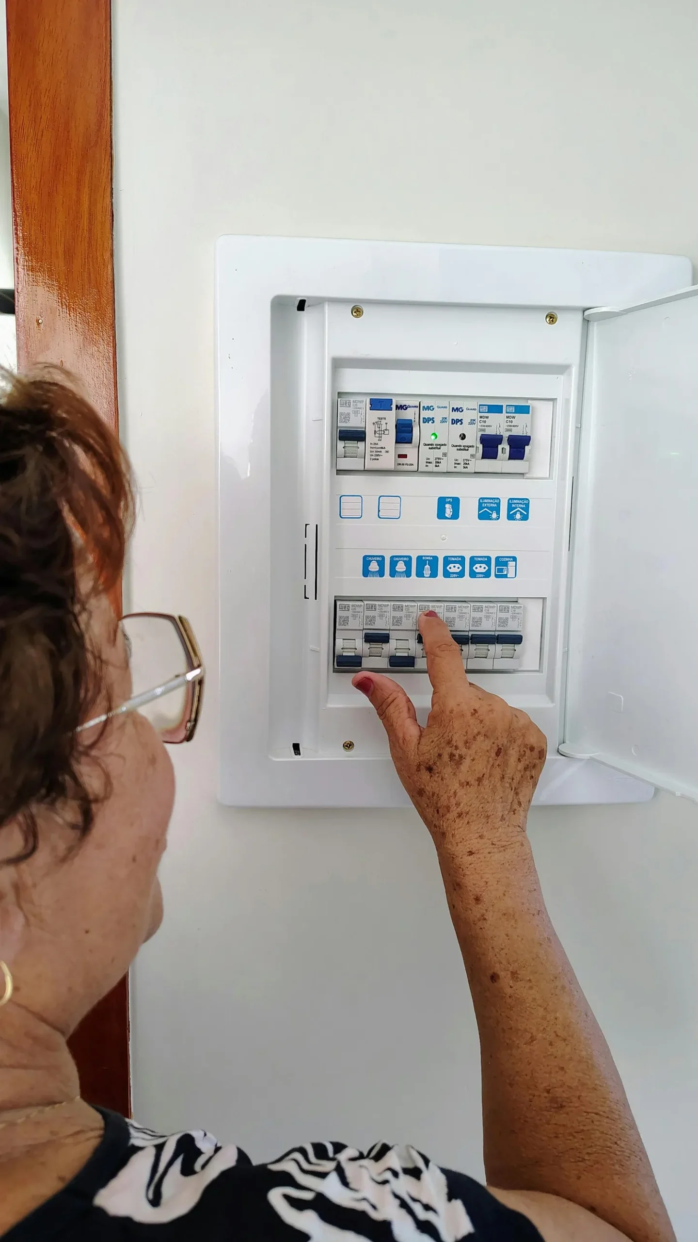 A woman interacting with an electrical control panel inside a house, showing hands-on operation.