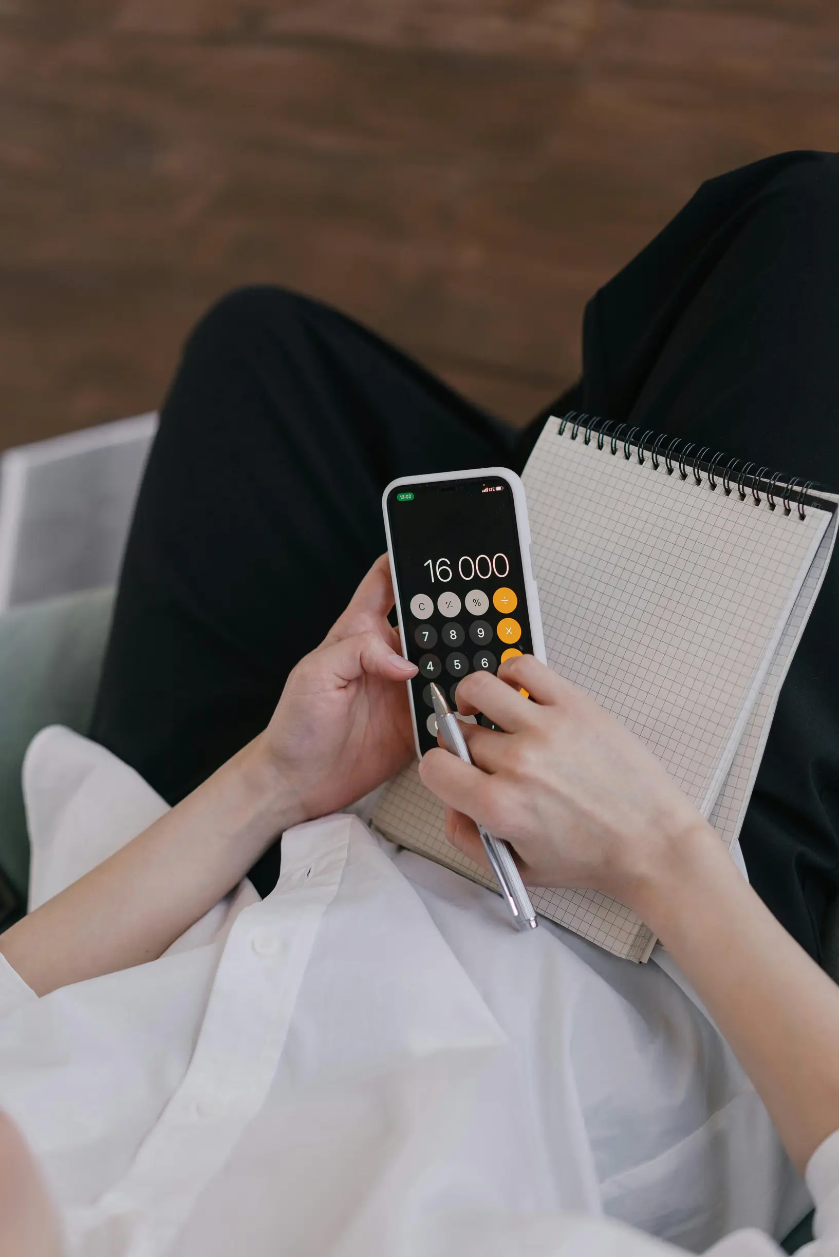 Close-up of a person using a smartphone calculator while planning finances with a notebook.