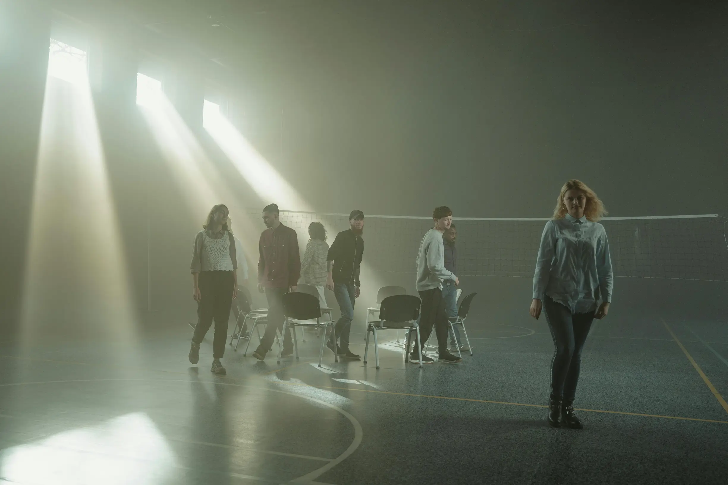 Group of people walking inside a smoky room with dramatic sunrays streaming through windows.