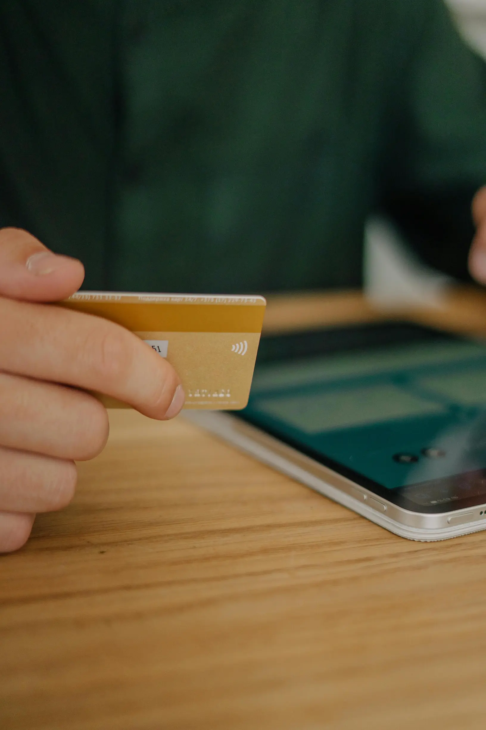 Person holding a credit card, making a contactless payment on a tablet indoors.