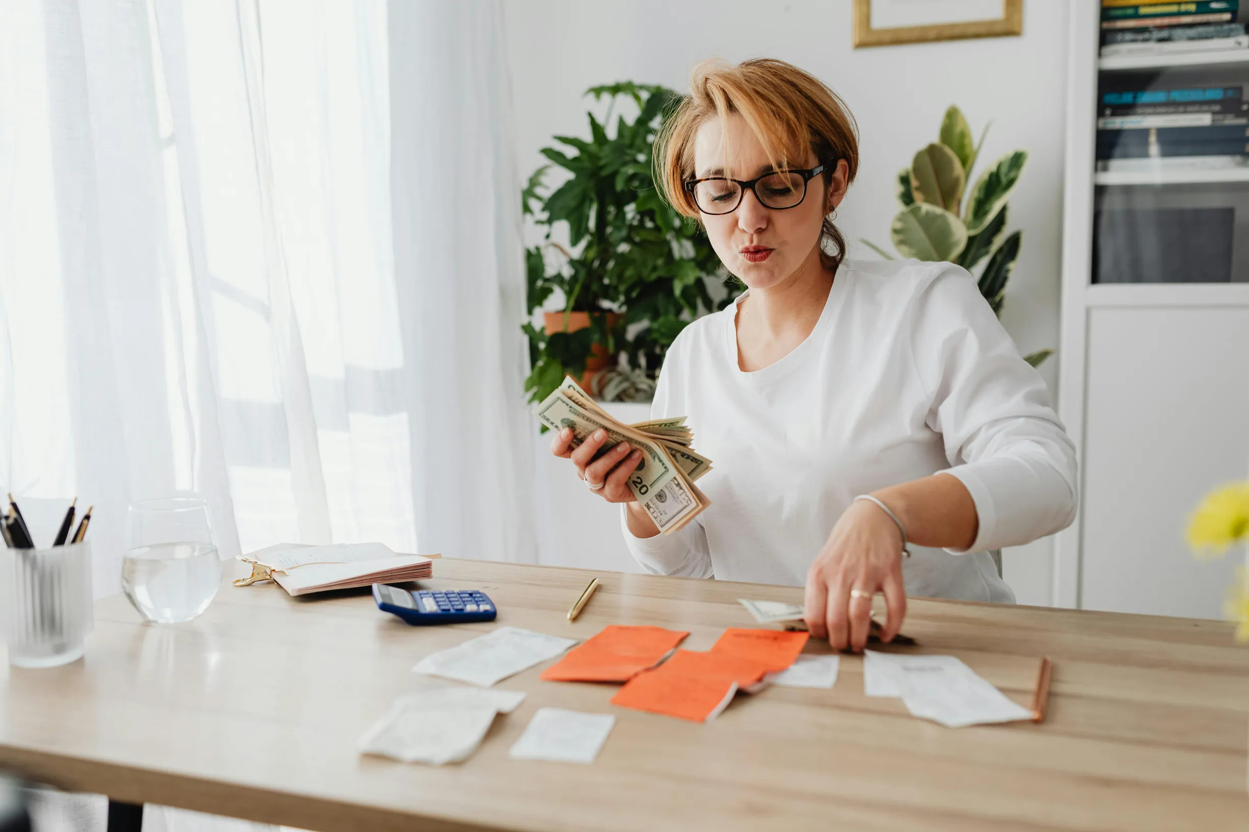 Woman sitting at a table counting cash and organizing receipts with a calculator nearby.