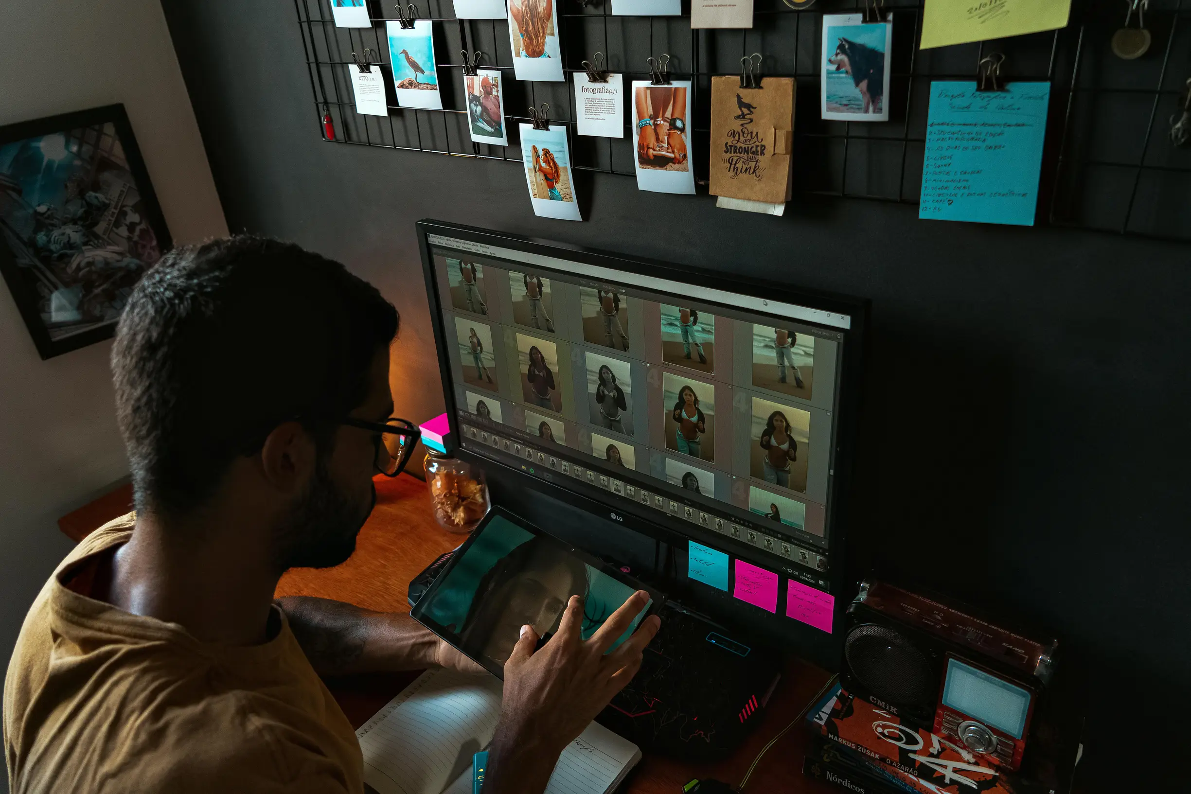 A young man edits photographs on a computer in a cozy home office setup.