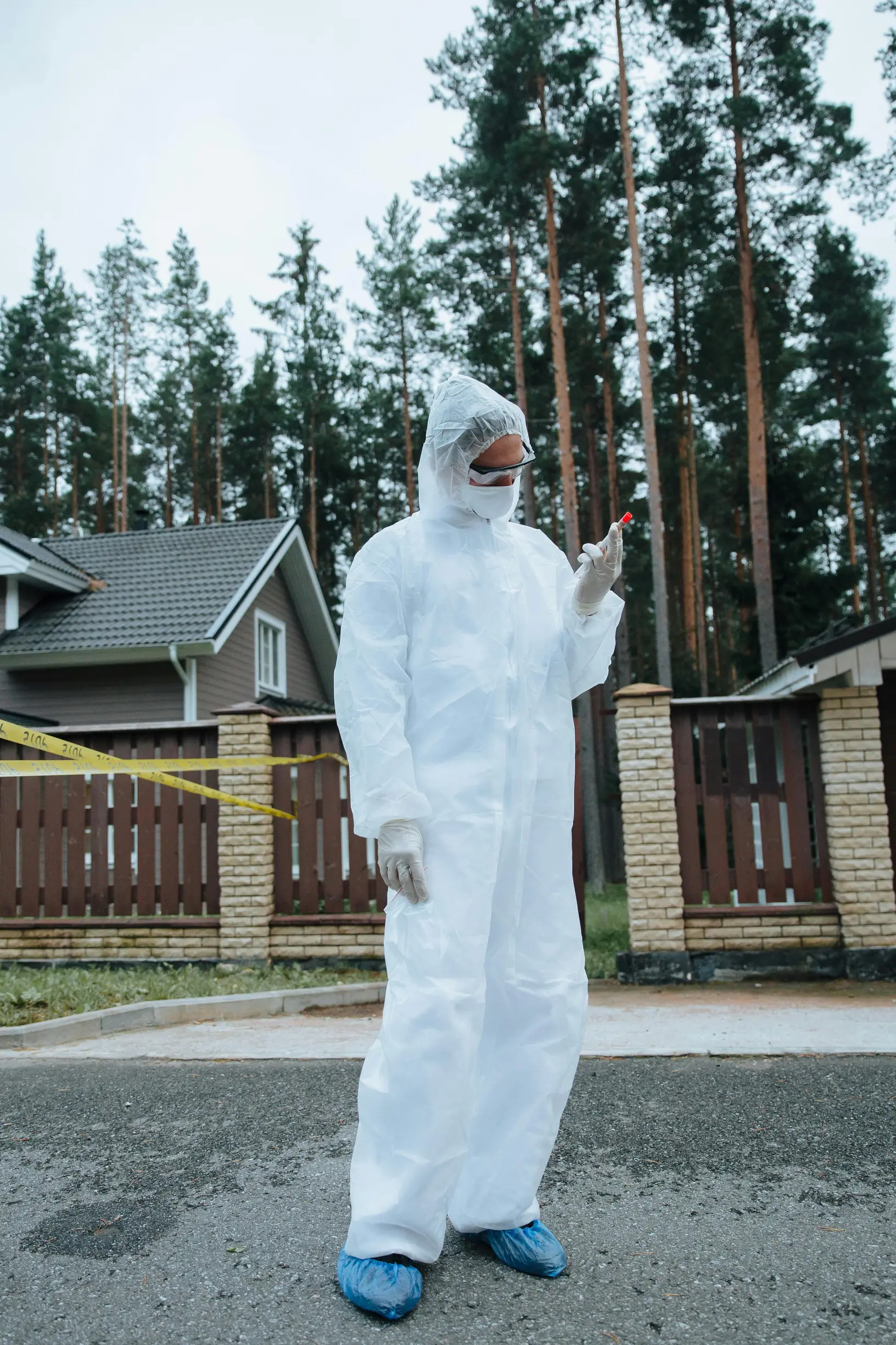 Forensic scientist in protective gear examines evidence at an outdoor crime scene.