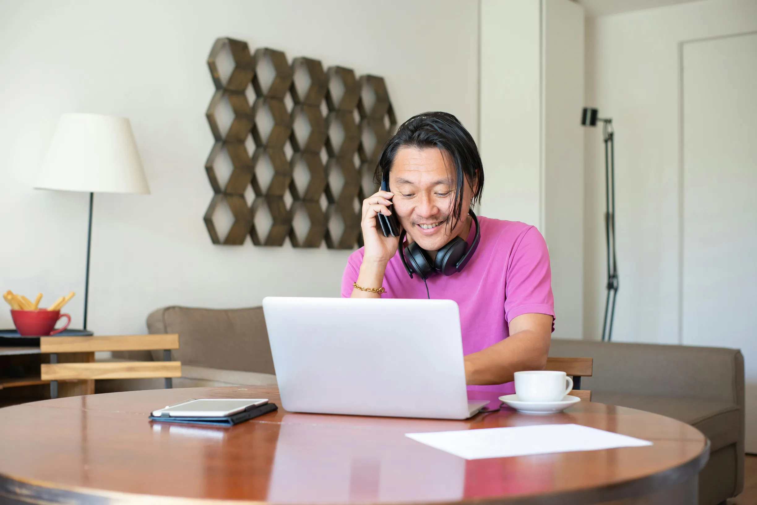 Man multitasking with phone and laptop in a cozy home setting, enjoying remote work flexibility.